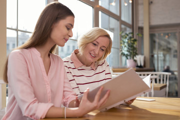 Great project. Attractive smiling granny discussing family business with her granddaughter while sitting at the table