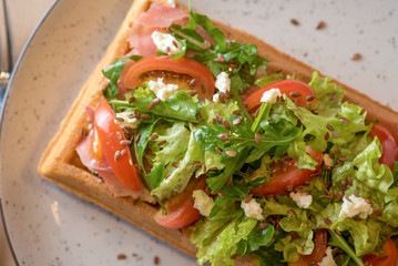 Fototapeta na wymiar Savory Belgian waffles with salmon, salad and tomato. Perfect breakfast for long day. Restaurant menu or recipe concept