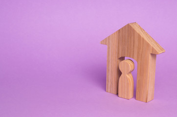 Wooden figurine of a man in a house on a purple background. The concept of an apartment house, real...
