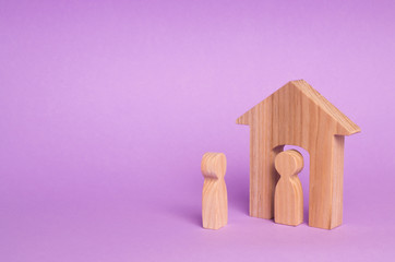 Obraz na płótnie Canvas A wooden figure of a man meets a guest on a purple background. Wooden house. The concept of an apartment house, real estate. Buying and selling apartments, affordable housing for families. Protection.