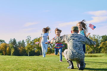 Soldier is meeting his family outdoors. Happy reunion of father and kids on the grass.