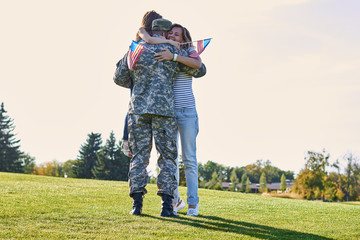 Military man father hugs daugther and wife. Portrait of happy american family with father us soldier. Sunny park meadow.