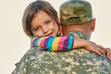 Family members welcomed back. Soldier father is hugging his daughter outside, family reunion.