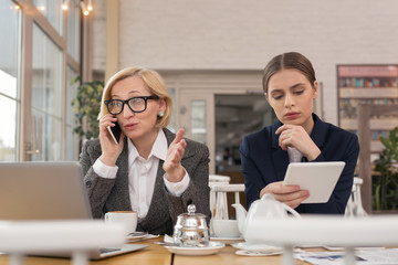 Talking with partner. Successful old businesswoman talking on the phone and her intern holding at...