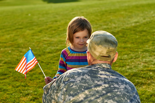 Daughter with american flag and her daddy. Love concept of soldier and little girl outdoors.