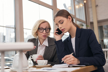 Leading business. Determined young businesswoman talking on the phone and taking notes