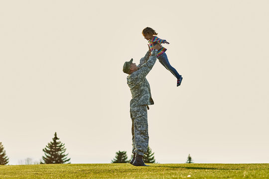 Soldier lifting up little kid. Father in military uniform is playing with daughter in the park.