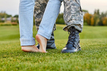 Close up soldier boots and girlfriend with naked feet. Standing on the grass.