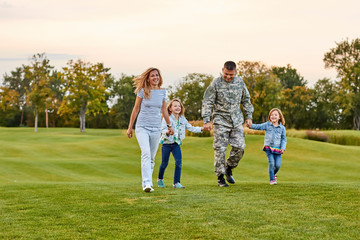 Happy family walking on the grass. Soldier with his wife and daughters in the park.