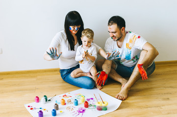 happy family son with parents and a cat painting a poster and one another with paints