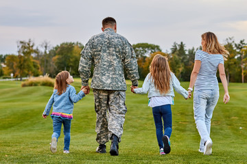 Back view soldier's family walking. Soldier at vacation. Four family members walking together holding hands.