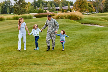 Obraz premium Soldier walking with kids and wife. Holding hands, happy reunion of father and his family. Walk on the grass.