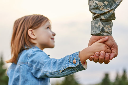 Soldier holding hand of little girl, close up. Hands of father and daughter. - Powered by Adobe