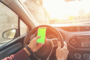 An unidentified man sitting at the wheel of car and holding smartphone with green screen. Chroma key. Copy space