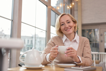 Pleasant day. Charming blond woman sitting in a cafe and drinking tea