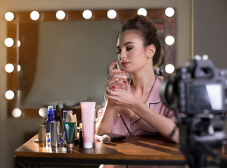 Great aroma. Young female blogger is sitting at dressing table and recording video for her beauty blog. She is smelling perfume with closed eyes
