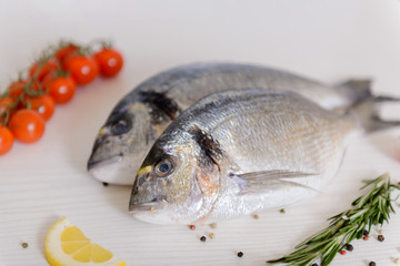 Two fresh dorada fishes with cherry tomatoes, rosemary, lemon and pepper on light wooden background...