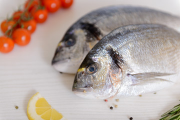 Two fresh dorada fishes with cherry tomatoes, rosemary, lemon and pepper on light wooden background...