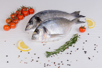 Two fresh dorada fishes with cherry tomatoes, rosemary, lemon and pepper on light wooden background
