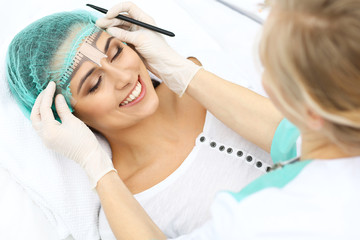 Professional beautician is going to correct eyebrow line at woman face using cosmetic ruler....