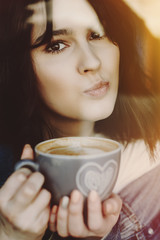 Close up portrait of cute young girl doing funny face while drinking a cup of coffee in a coffee shop.