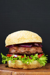 Fresh and delicious home made burger on wooden board with copy space. Closeup.