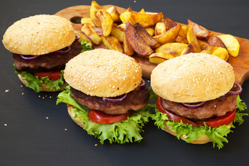 Fresh burgers with fried potatoes on wooden board. Side view.