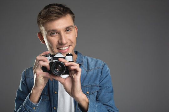 Portrait of happy guy standing with old camera in arms and making snapshot. Copy space in right side. Isolated on background