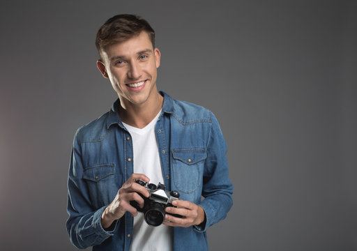 Waist up portrait of enjoyed handsome man standing with retro camera in hands and smiling. Copy space in right side. Isolated on background