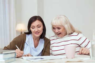 Fun together. Joyful elder woman and caregiver reading news and having fun