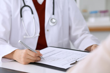 Close up of a female doctor filling up  an application form while consulting patient