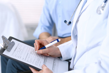 Female doctor holding application form while consulting man patient in hospital. Medicine and...