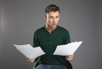 Waist up portrait of shocked male person taking seat on chair and looking at papers in his hands...