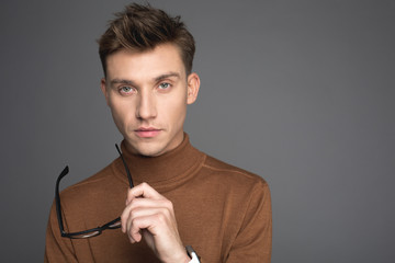 Portrait of young guy holding glasses in hand and looking at camera with seriousness. Copy space in right side. Isolated on background