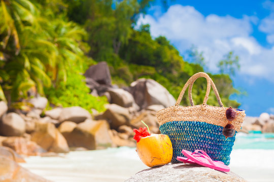 Straw bag, sun glasses, coconut and pink flip flops on a tropical beach