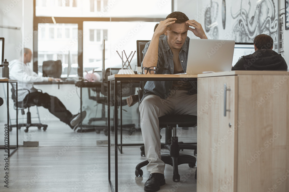 Poster full length portrait of undeceived man looking at notebook computer while sitting at table. disillus