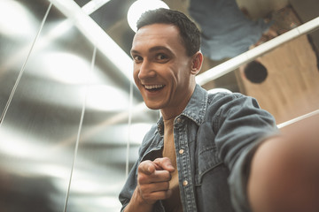 Portrait of laughing male doing selfie while looking at camera. He locating in elevator....