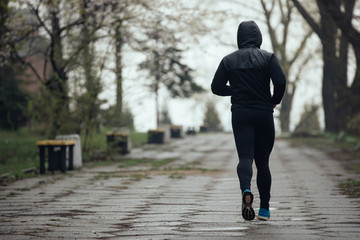 Sports man jogging outdoors in rainy day, back view
