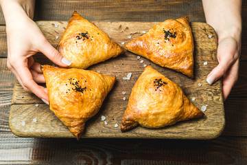 Uzbek national dish of samsa on a wooden board in the hands of a girl