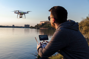 Man operating / flying with drone by the river at sunset , closeup and back view shot  - obrazy, fototapety, plakaty