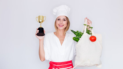 woman in cook uniform holding with different vegetables and prize cup
