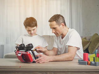 Cheerful father is repairing toy vehicle of his son. Child is watching how parent using tool with interest