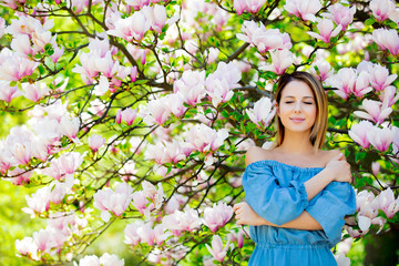 Young redhead girl in blue dress in springtime blossom magnolia garden.