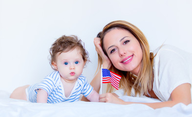 Young mother and little child boy lying down in white bed and holding american flag