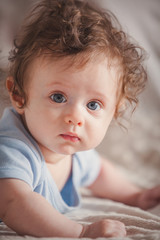 Little curly child boy lying down in bed. Side corner view