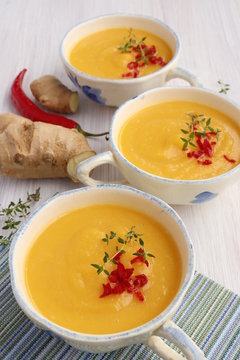 Pumpkin puree soup in cups with chili pepper and thyme