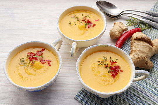Pumpkin puree soup in cups with chili pepper and thyme