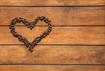 Top view close up heart-shaped aromatic coffee beans locating on wooden desk. Copy space