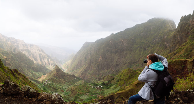 Traveler on the mountain edge making a photo of landscape. Deep clouds above green Xo-Xo Valley. Santo Antao Island, Cape Verde