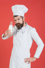 Cook, chef with confident face in white uniform has bottle of fresh milk. Protein diet concept - bearded man with milkshake, milk or yogurt. Man with beard and mustache holds glass bottle milk drink.
